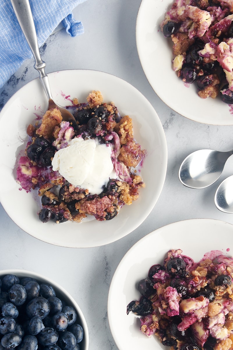 Overhead view of blueberry crisp on 3 white plates, center with scoop of vanilla ice cream