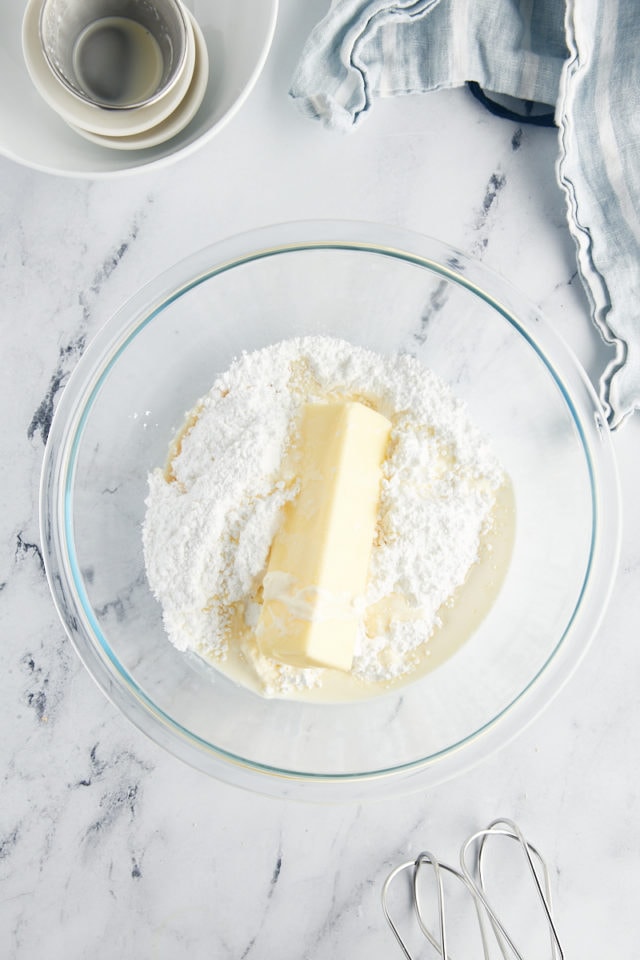 overhead view of butter, powdered sugar, cream, vanilla, and salt in a glass mixing bowl