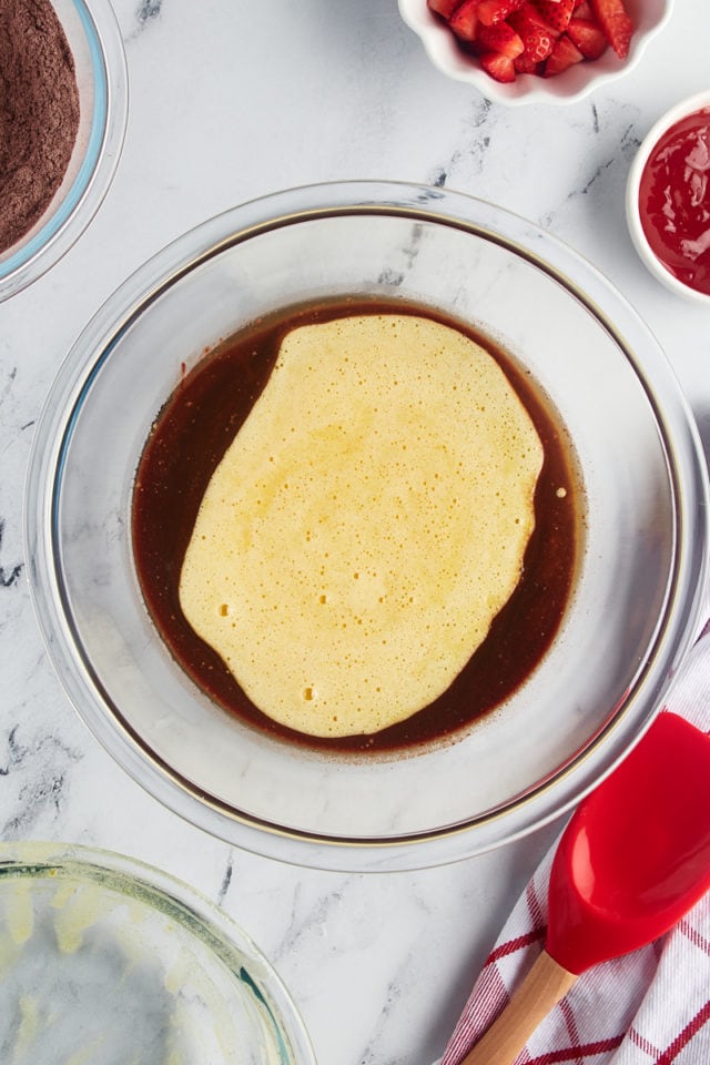 Overhead view of egg and liquid ingredients added to bowl of melted chocolate and butter