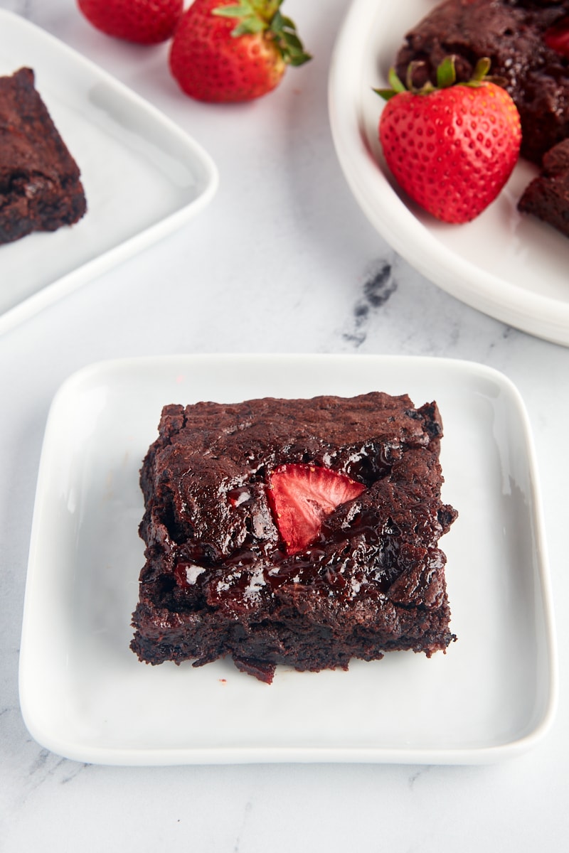 Strawberry brownie on plate with additional brownies and fresh berries in background