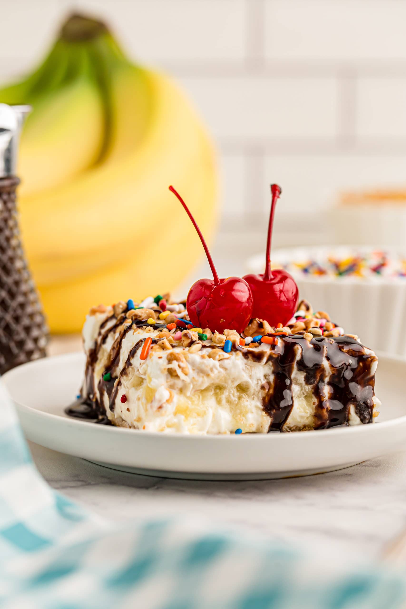 Side view of banana split cake on plate topped with 2 cherries