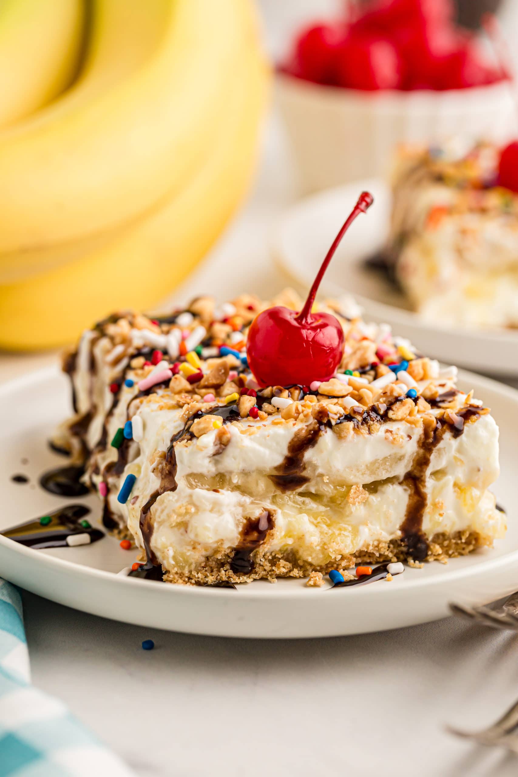 Slice of banana split cake topped with cherry and chocolate syrup