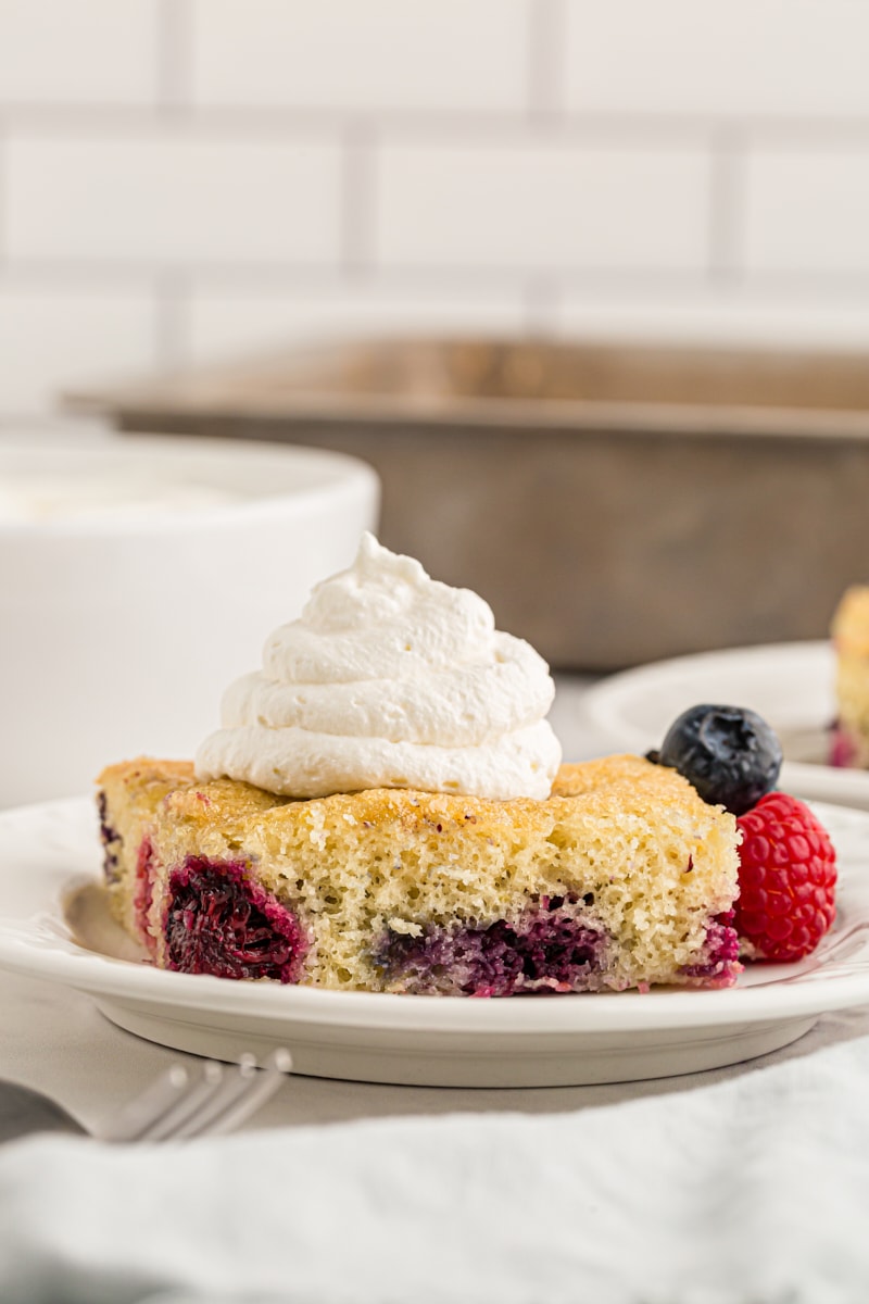 a slice of berry pudding cake topped with whipped cream and served on a white plate