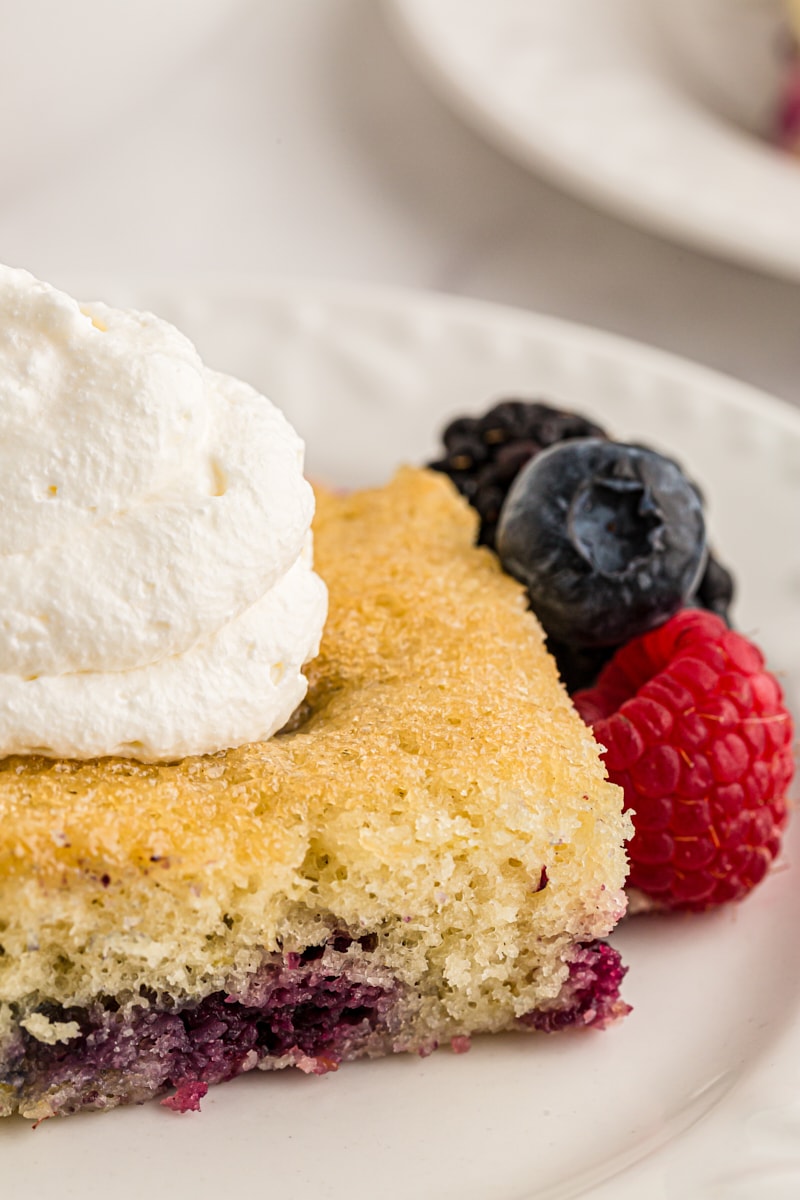 close up view of a slice of berry pudding cake topped with whipped cream