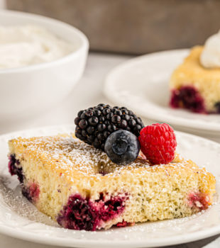 a slice of berry pudding cake topped with fresh berries