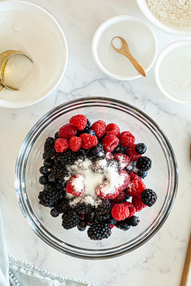 overhead view of berries and sugar in a glass mixing bowl