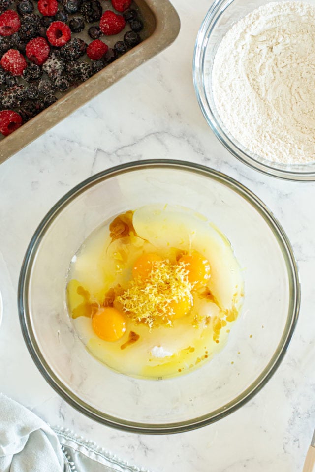 overhead view of sugar, eggs, olive oil, lemon zest, and vanilla extract in a glass mixing bowl