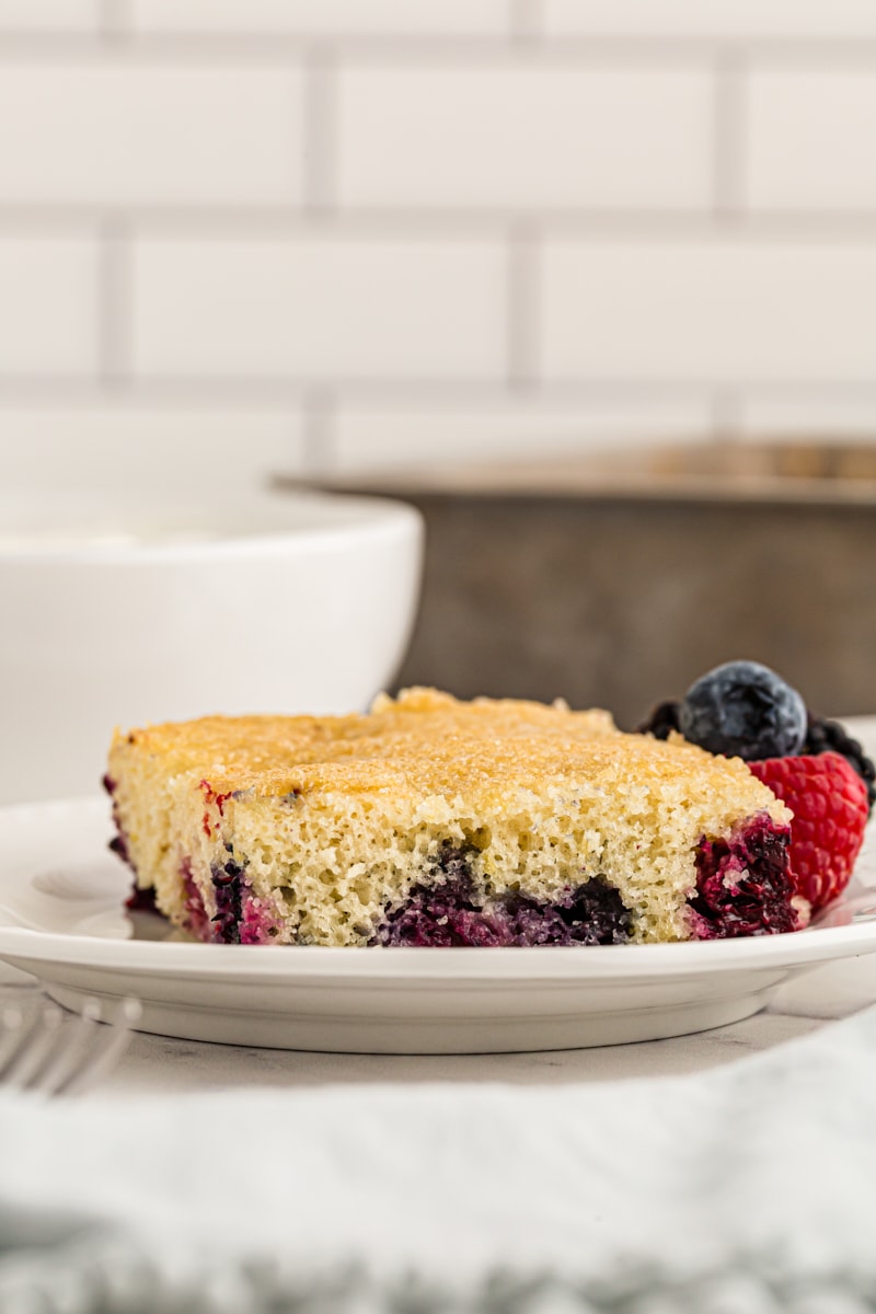 a slice of berry pudding cake on a white plate and served with fresh berries