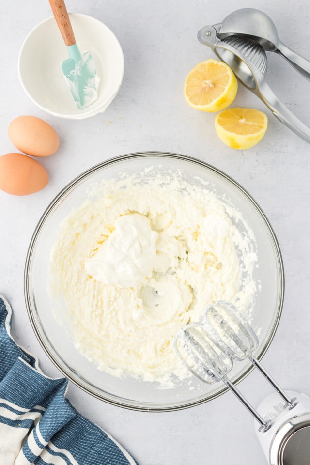 overhead view of sour cream added to creamed butter and sugar in a glass mixing bowl