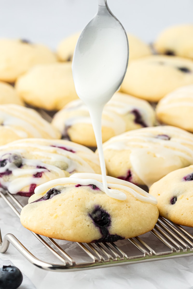 lemon glaze being drizzled over lemon blueberry cookies on a wire rack