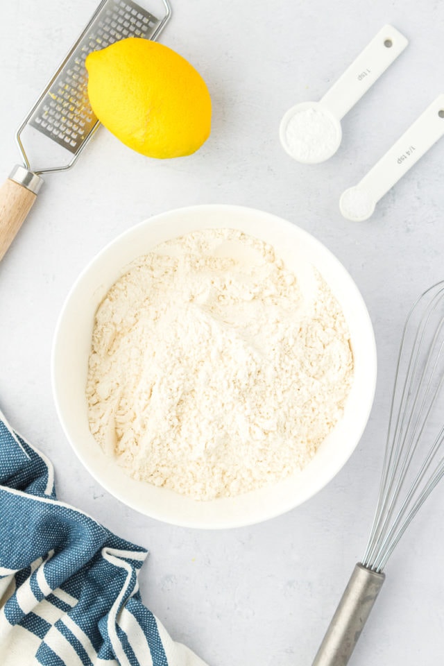 overhead view of flour, baking powder, salt, and lemon zest in a white mixing bowl