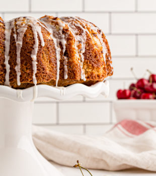 Whole cherry-vanilla yogurt cake on cake stand with glaze dripping down sides