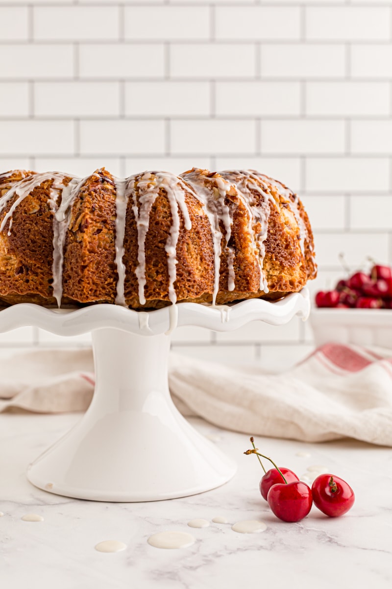 Whole cherry-vanilla yogurt cake on cake stand with glaze dripping down sides