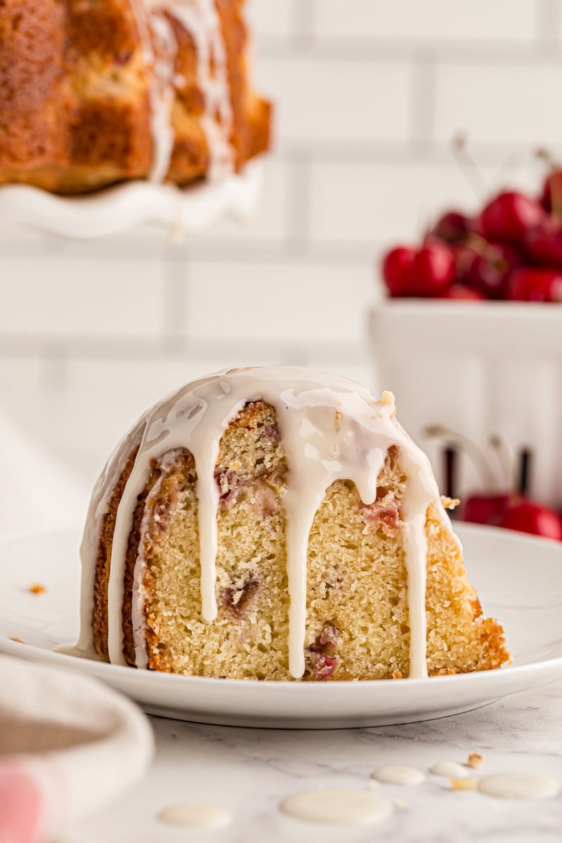 Slice of moist cherry-vanilla yogurt cake on plate with glaze dripping down sides