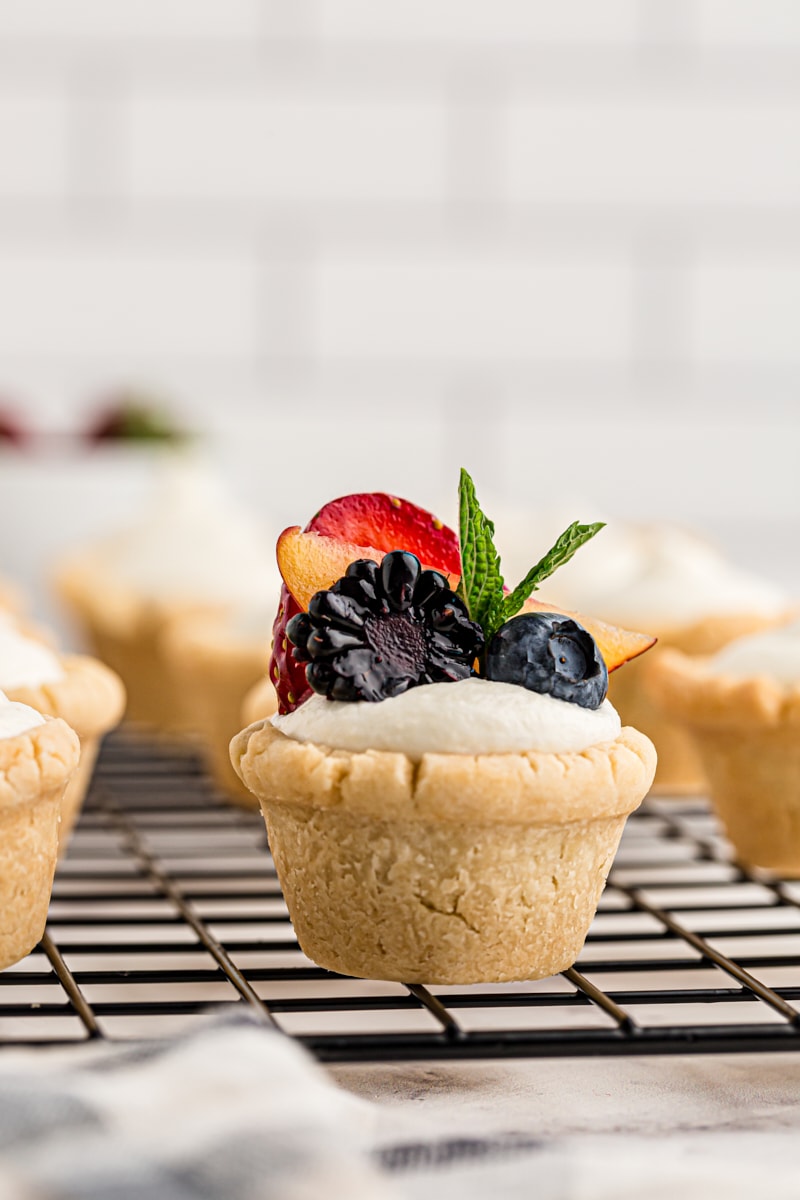 a mini fruit tart topped with pieces of strawberry, peach, blackberry, blueberry, and a mint leaf sprig