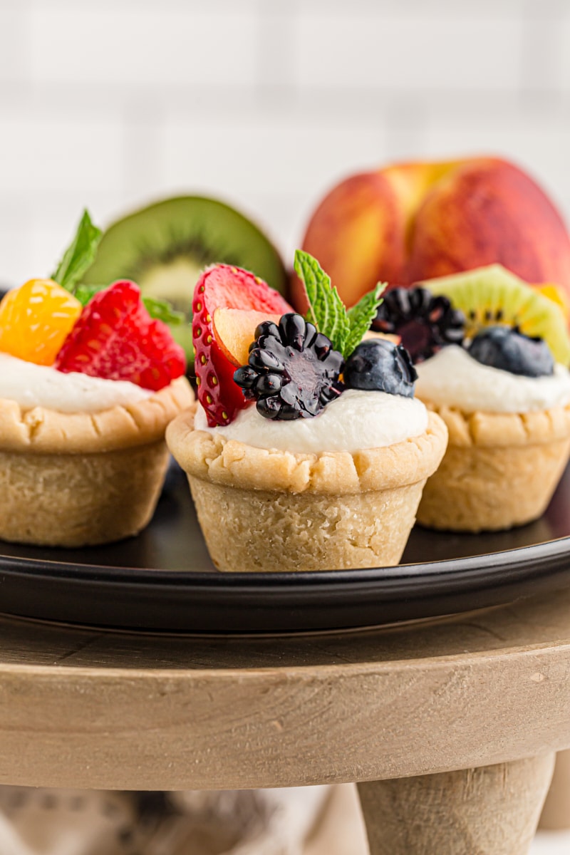 mini fruit tarts on a black tray on top of a wooden pedestal