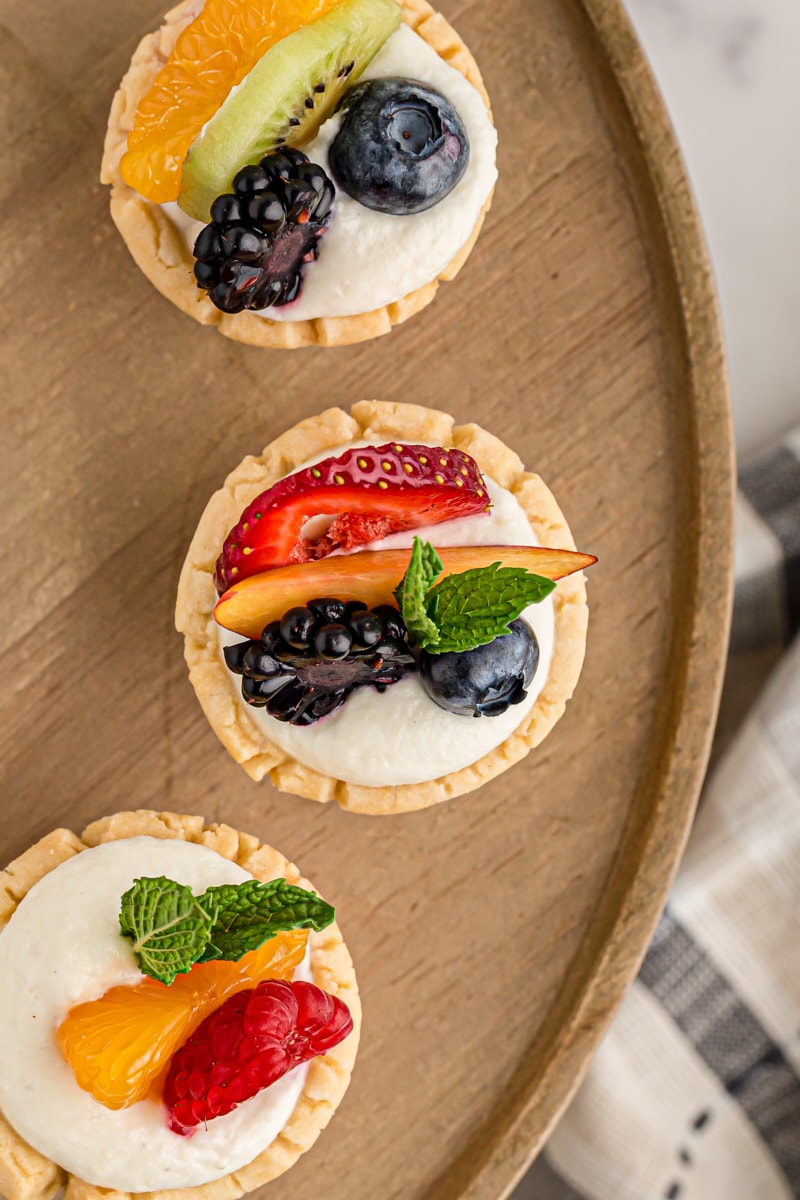overhead view of three mini fruit tarts on a wooden tray
