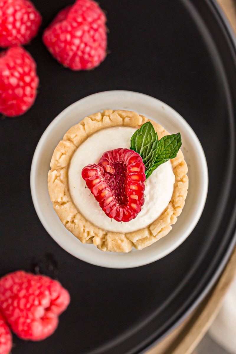 overhead view of a mini fruit tart topped with a fresh raspberry and a sprig of mint