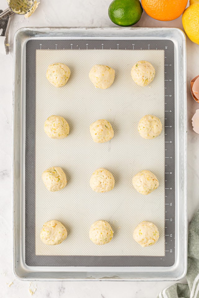 overhead view of portioned citrus cookie dough on a baking sheet lined with a silicone mat