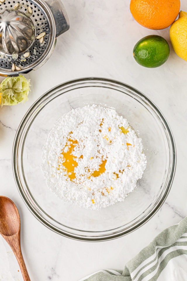 overhead view of confectioners sugar and citrus juices in a glass mixing bowl
