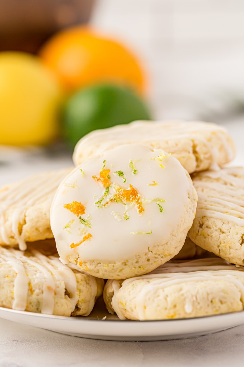 glazed Triple Citrus Cookies on a white plate with a lemon, lime, and orange in the background