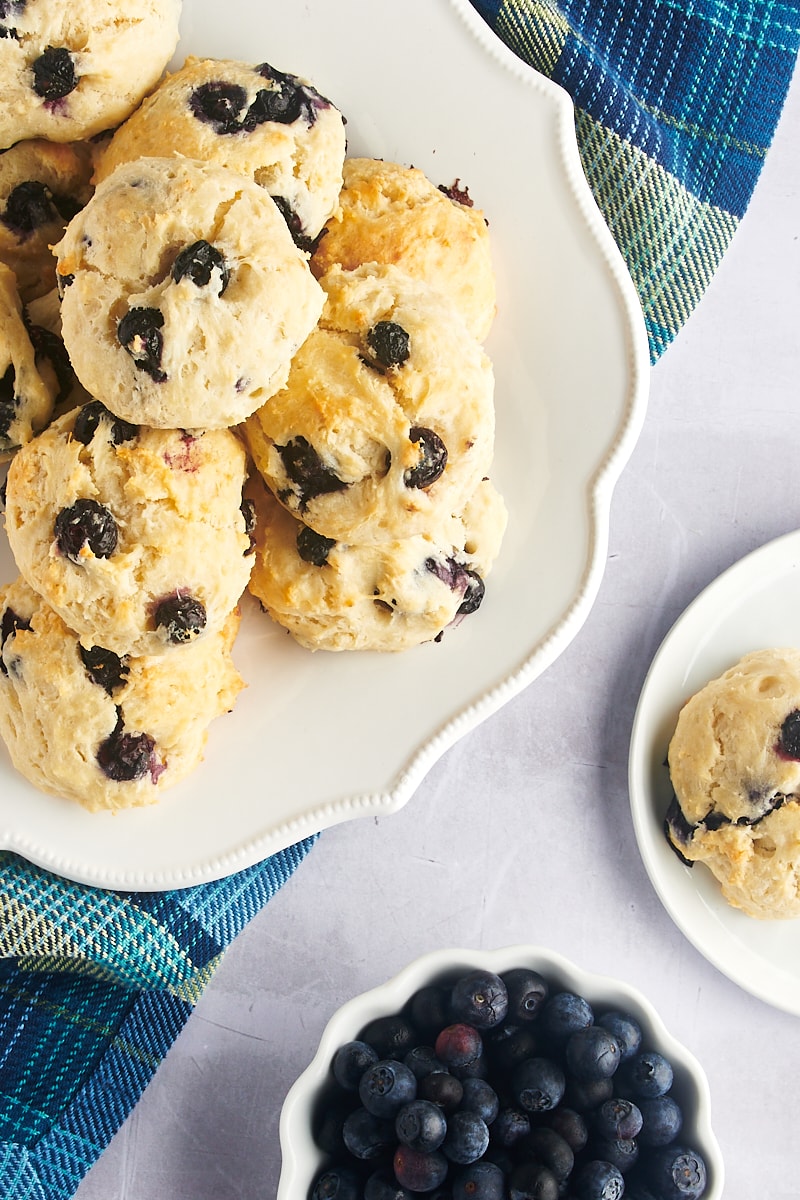 Overhead view of blueberry biscuits on platter and plate, with bowl of blueberries