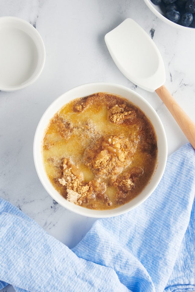 overhead view of graham cracker crumbs, melted butter and brown sugar in a white mixing bowl