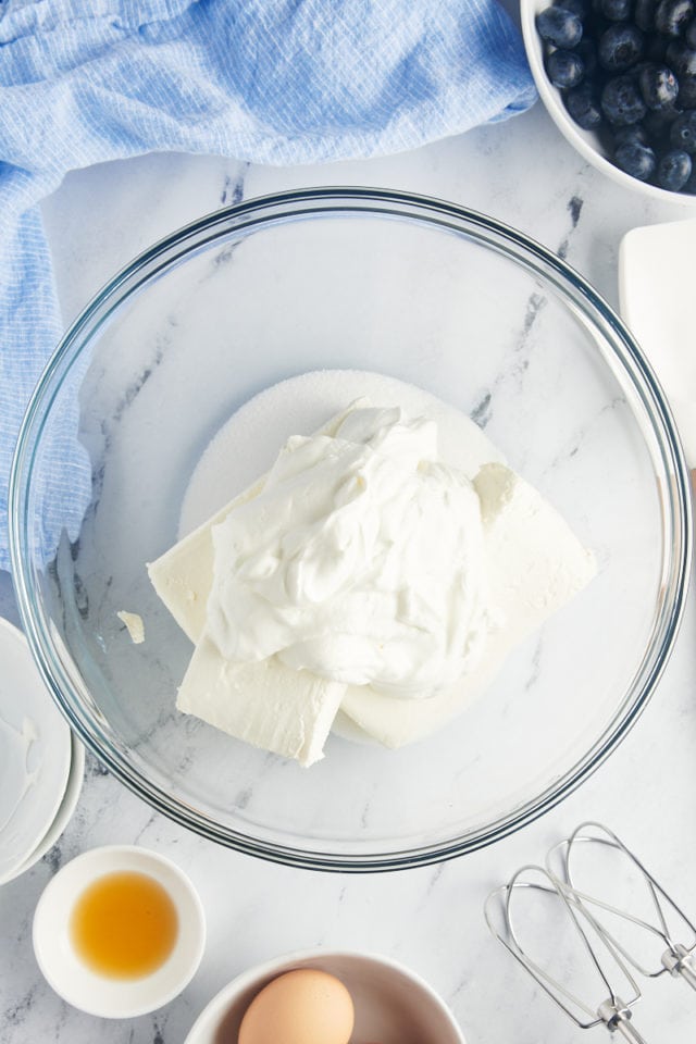 overhead view of cream cheese, sugar, and sour cream in a glass mixing bowl