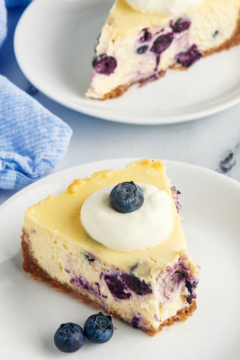 a slice of blueberry cheesecake topped with whipped cream and blueberries 