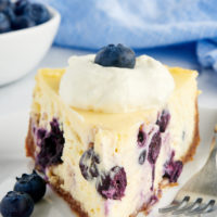 a close up of a slice of blueberry cheesecake on a white plate