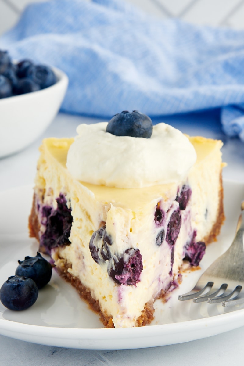 a close up of a slice of blueberry cheesecake on a white plate