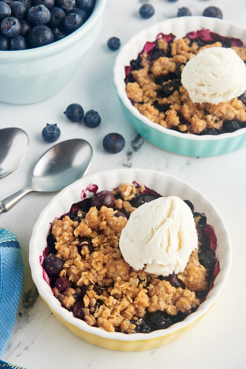 Two small baking dishes of blueberry crumble topped with scoops of vanilla ice cream