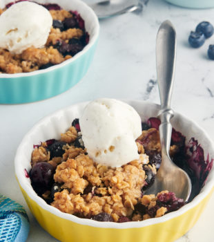 Two small dishes of blueberry crumble with vanilla ice cream