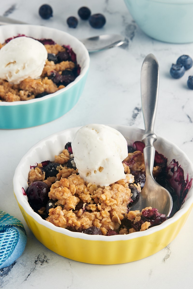 Two small dishes of blueberry crumble with vanilla ice cream