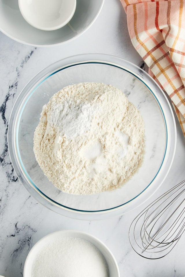 overhead view of flour, baking powder, baking soda, and salt in a glass mixing bowl