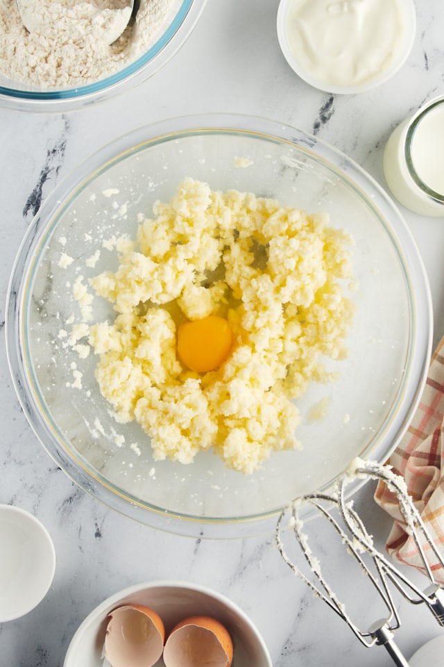overhead view of an egg and almond extract added to creamed butter and sugar in a glass mixing bowl