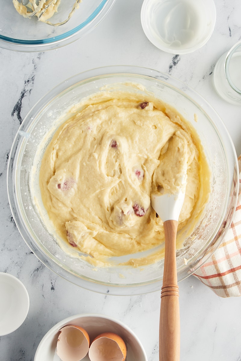 The completed raspberry coffee cake batter in a glass mixing bowl, with berries evenly distributed.