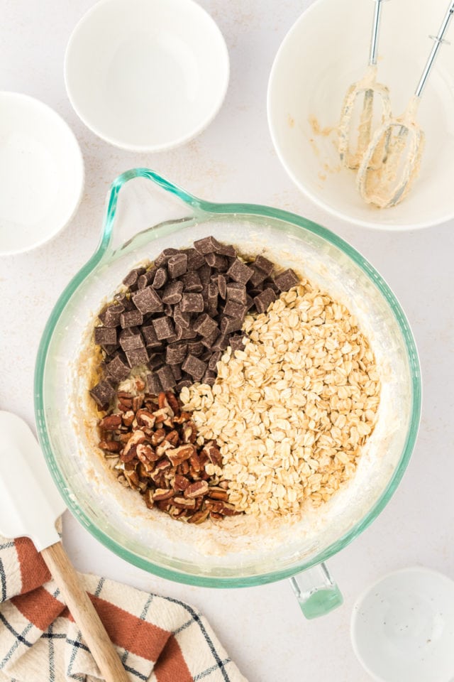 Overhead view of oats, chocolate chunks, and pecans added to bowl of dough