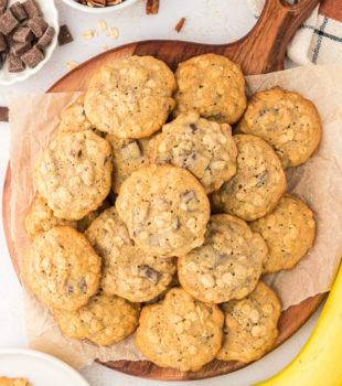 Overhead view of banana pecan chocolate chunk cookies on parchment-lined wood board