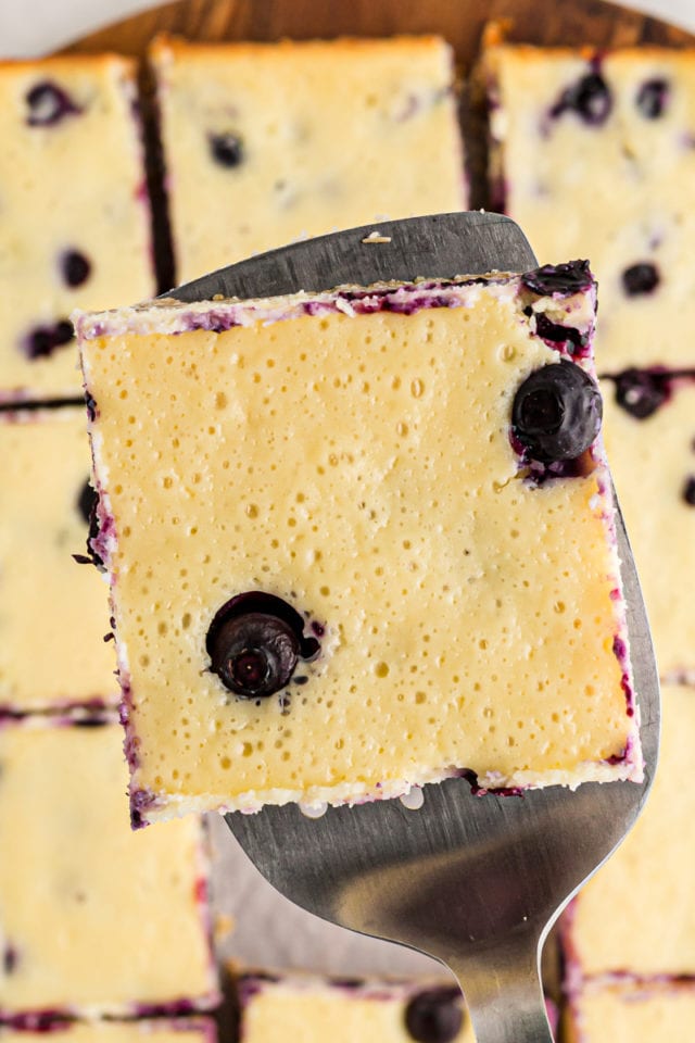 Blueberry oat cheesecake bar held on spatula above cut bars on board