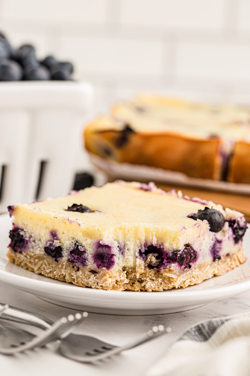 Blueberry oat cheesecake bar on plate with bite taken out of corner