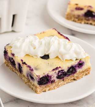 Blueberry oat cheesecake bar on plate with whipped cream on top