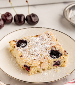 Cherry almond sheet cake on plate, with remaining cake and cherries in background