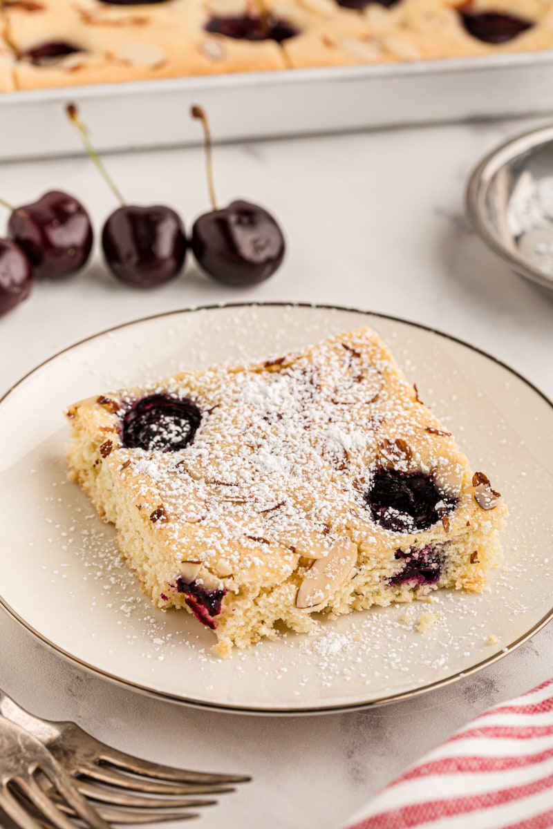 Cherry almond sheet cake on plate, with remaining cake and cherries in background
