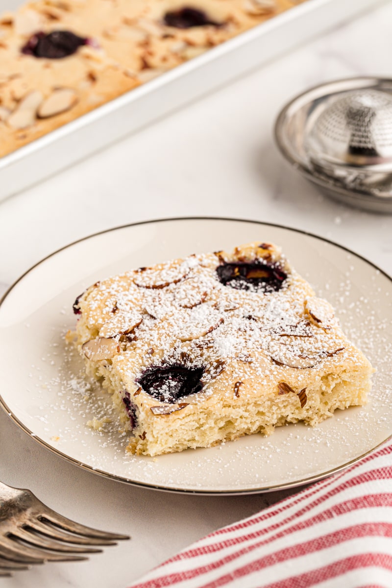 Slice of cherry almond sheet cake on plate, dusted with powdered sugar