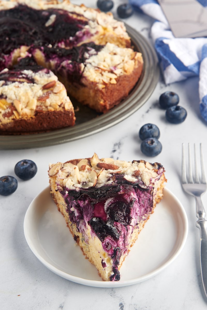 Slice of blueberry cream cheese coffee cake on plate with remaining cake in background