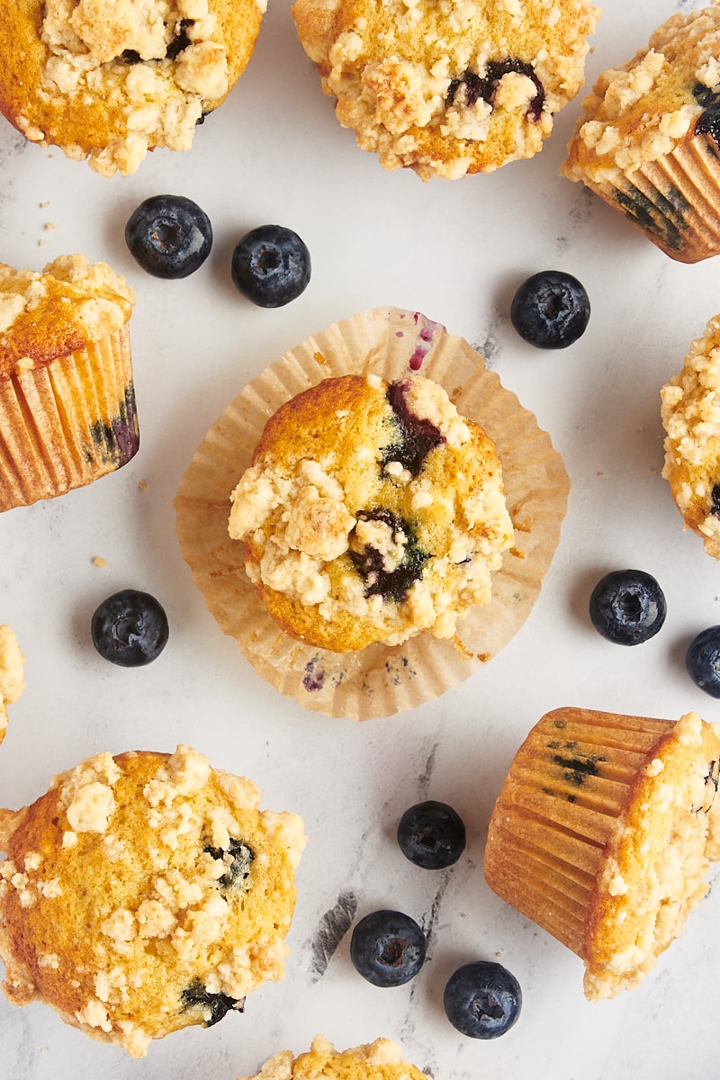 Overhead view of blueberry crumb muffins on countertop with middle muffin set on wrapper