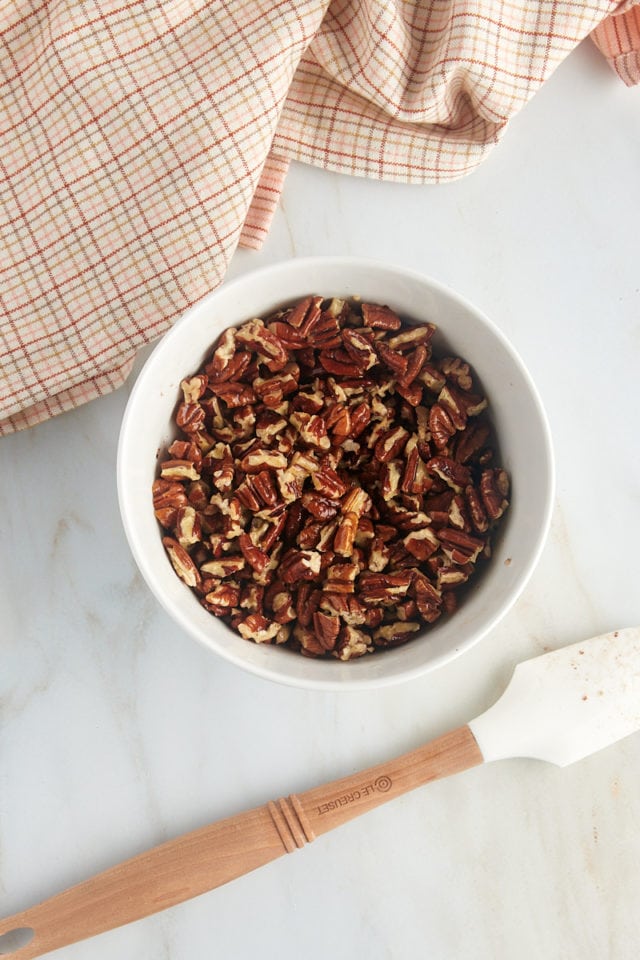 overhead view of chopped pecans mixed with melted butter in a white bowl