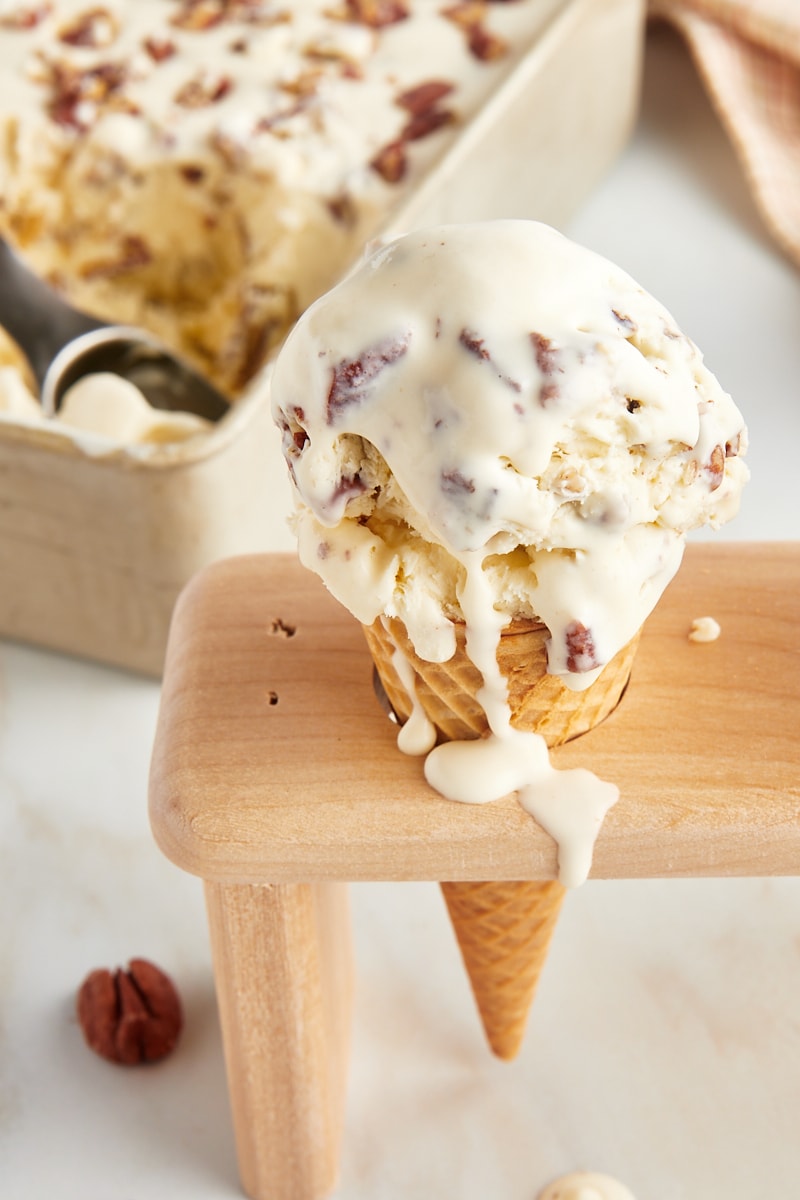 a waffle cone filled with butter pecan ice cream with more ice cream in the background