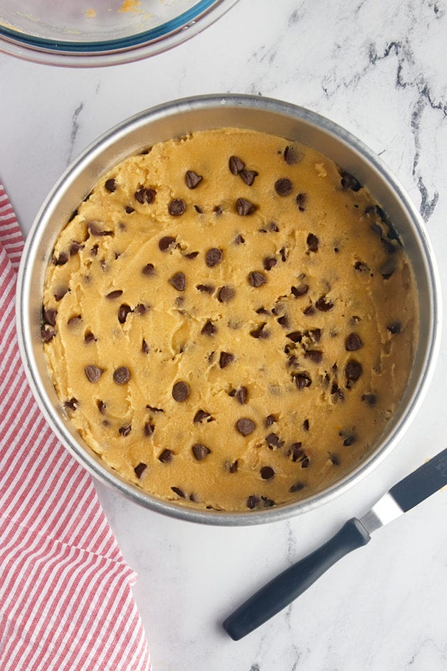 overhead view of chocolate chip cookie cake dough spread in a round cake pan